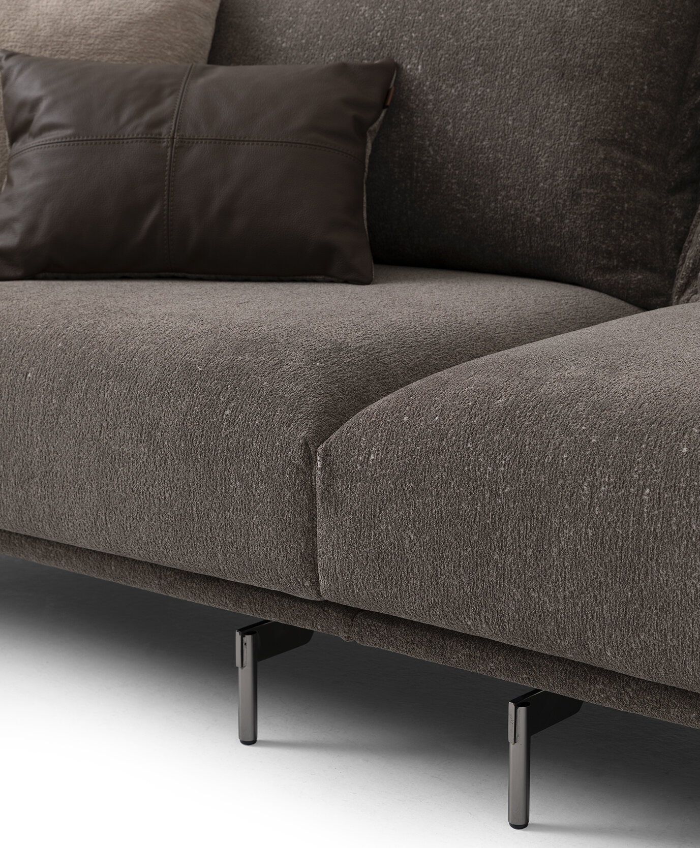 Modern dark grey fabric sofa with sleek black metal legs and a leather accent pillow, perfect for contemporary living room decor.