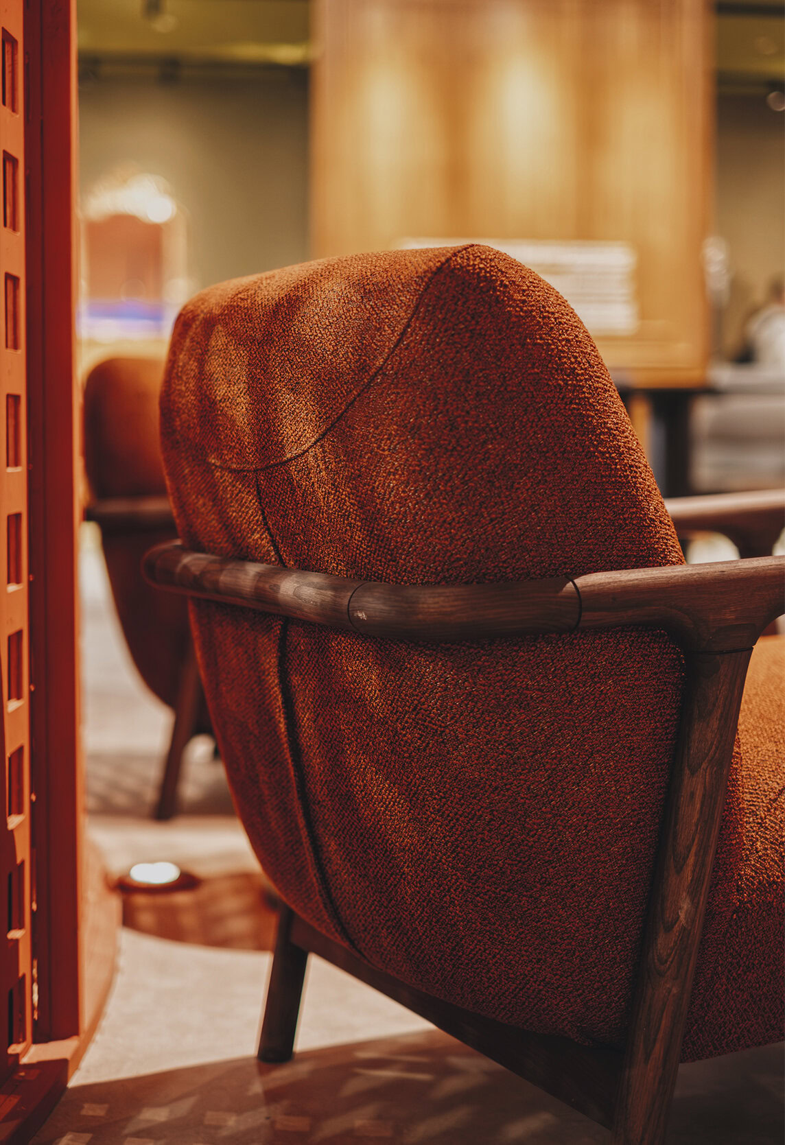 Elegant mid-century modern armchair with warm orange textured fabric and rich wooden armrests, perfect for stylish living or office spaces.